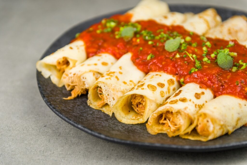Prato preto com panquecas recheadas com frango, regadas com molho de tomate e polvilhadas com salsinha picada