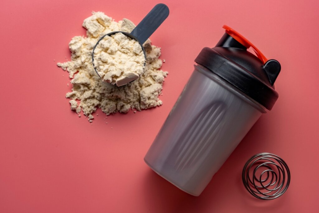 Imagem de uma colher dosadora com suplemento e um copo para o shake preto em fundo vermelho