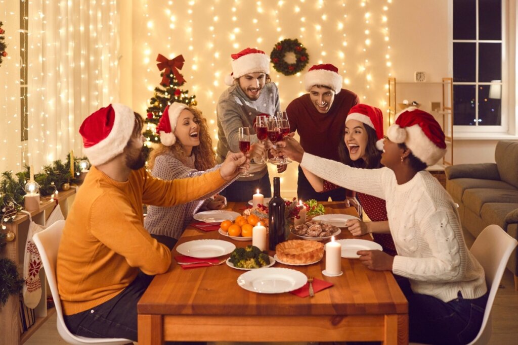 Pessoas reunidas ao redor de uma mesa com comidas celebrando o Natal e brindando com taças com vinho tinto