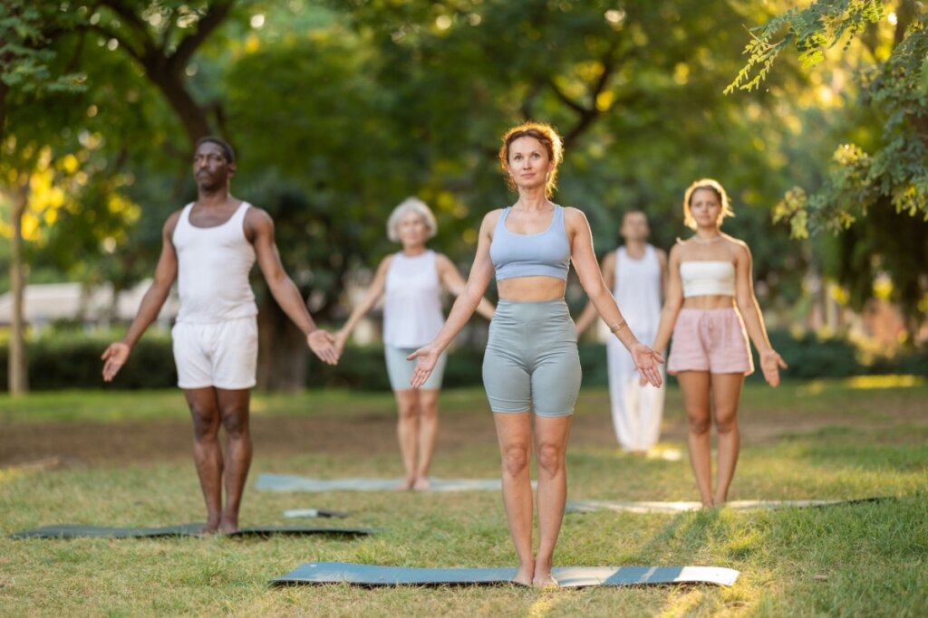 cinco pessoas em parque fazendo tadasana em cima de tapetes de yoga