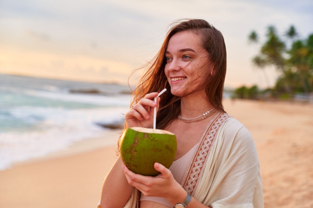 Mulher em uma praia, sorrindo e bebendo água de coco