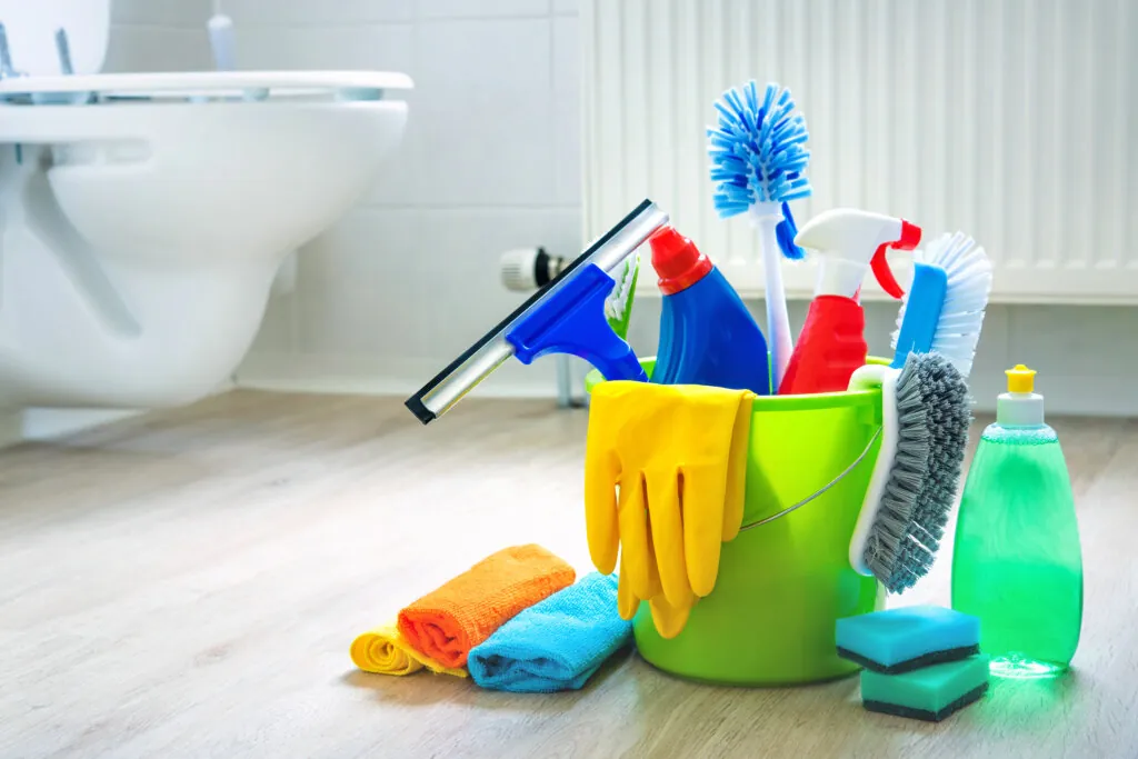 Produtos de limpeza em um balde verde no chão do banheiro