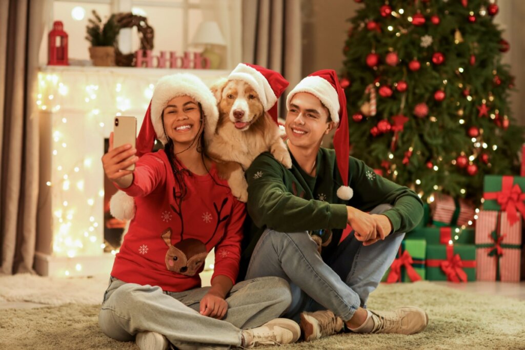 Casal tirando foto com um cachorro em frente a uma árvore de Natal