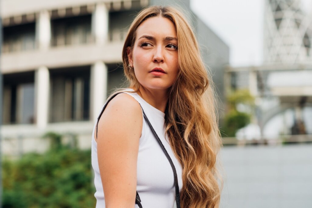 Mulher, com cabelo ruivo longo com ondas, virada de lado e usando blusa branca 