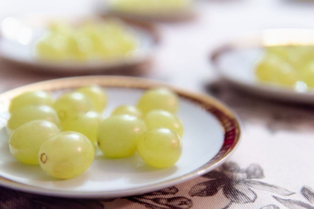 Prato branco com borda dourada com uvas verdes em cima 