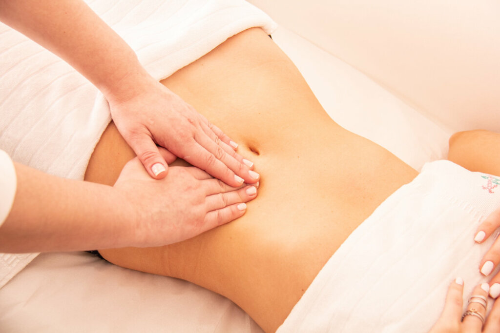 Mãos feminina fazendo massagem na barriga de uma mulher