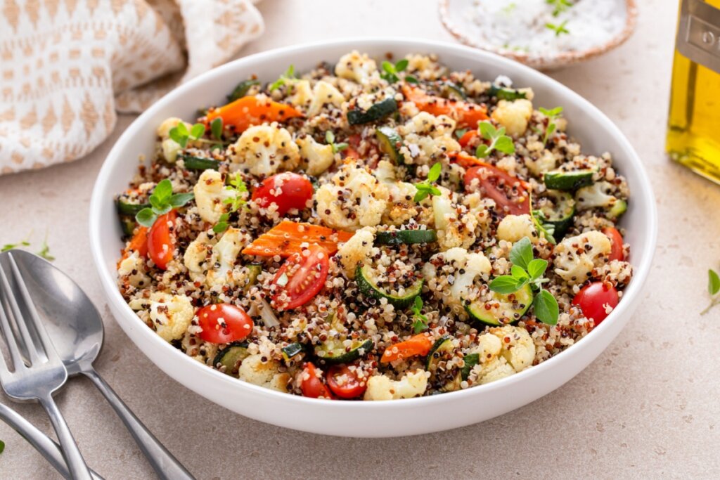 Salada de quinoa com couve-flor, cenoura, abobrinha, tomate-cereja e folhas de ervas frescas em recipiente branco