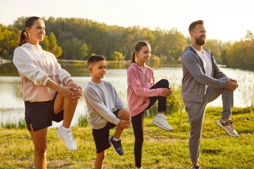 Pai, mãe e duas crianças em ambiente com lago alongando