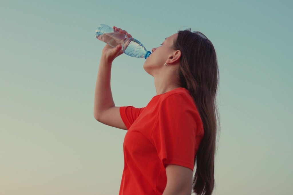 Mulher usando blusa vermelha, em pé ao ar livre, e bebendo água