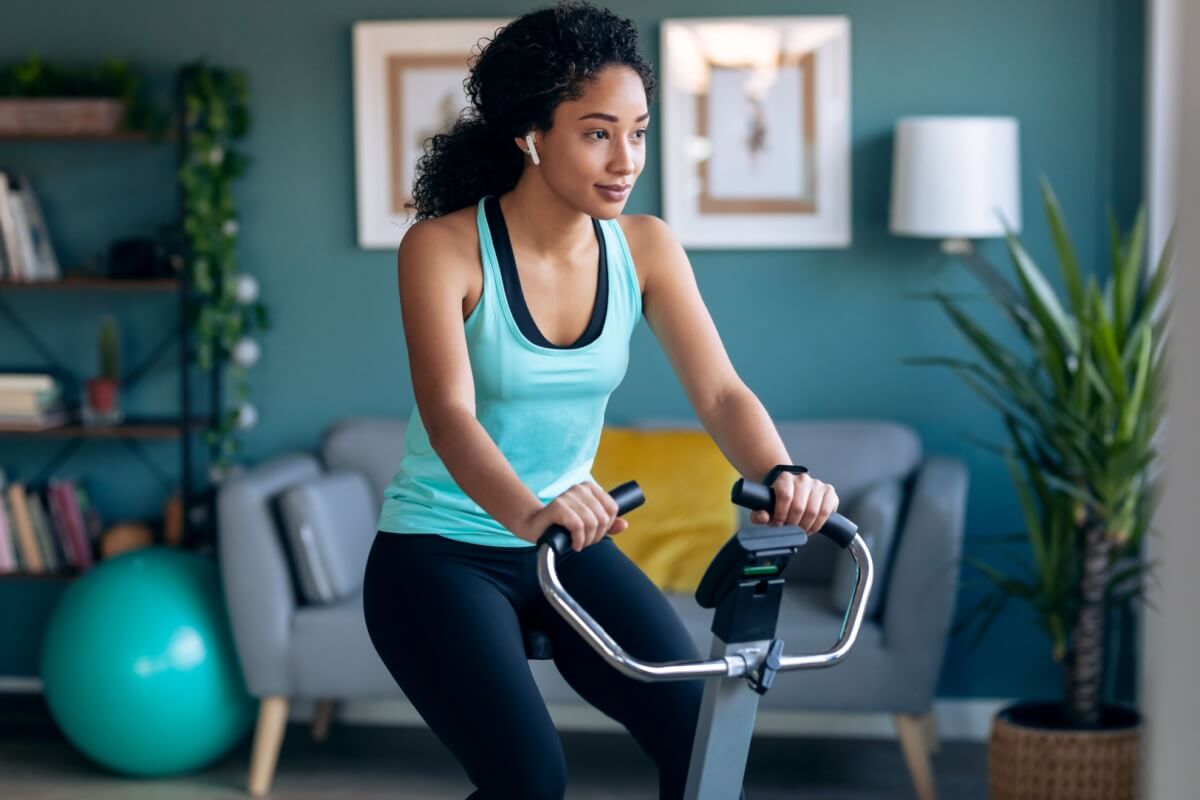 Jovem com o cabelo cacheado usando roupas de academia e fazendo exercício em bicicleta ergométrica