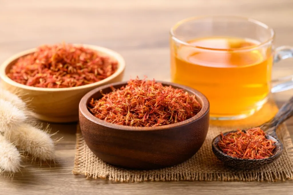 Tigelas com fios de cártamo secos dispostos sobre a mesa, ao lado de uma xícara com infusão da planta