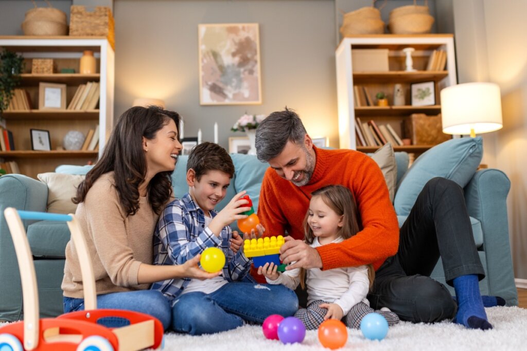 Mulher, homem e um menino e menina, sentados em um tapete na sala de estar, brincando de montar brinquedos 