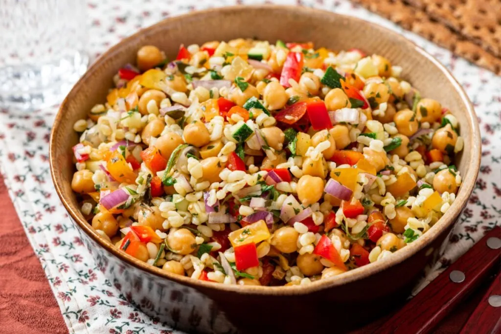 Recipiente preto com salada de grão-de-bico com bulgur, pimentão, feijão-preto, cebola-roxa e brotos de alfafa
