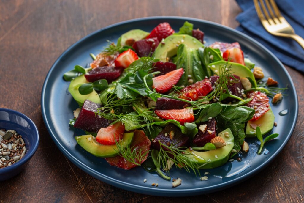 Prato azul com salada de folhas verdes com morango, beterraba, abacate e laranja sanguínea 