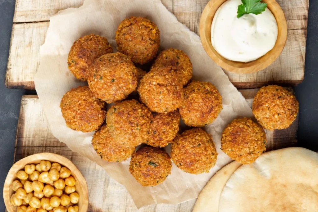 porção de falafel em cima de papel com molho branco ao lado e pote com grão-de-bico