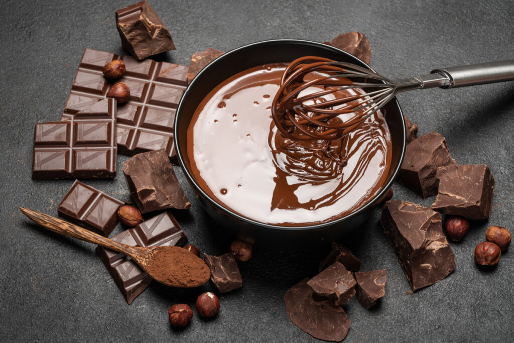 Chocolate derretido em recipiente preto e barras de chocolate rusticamente cortadas ao redor