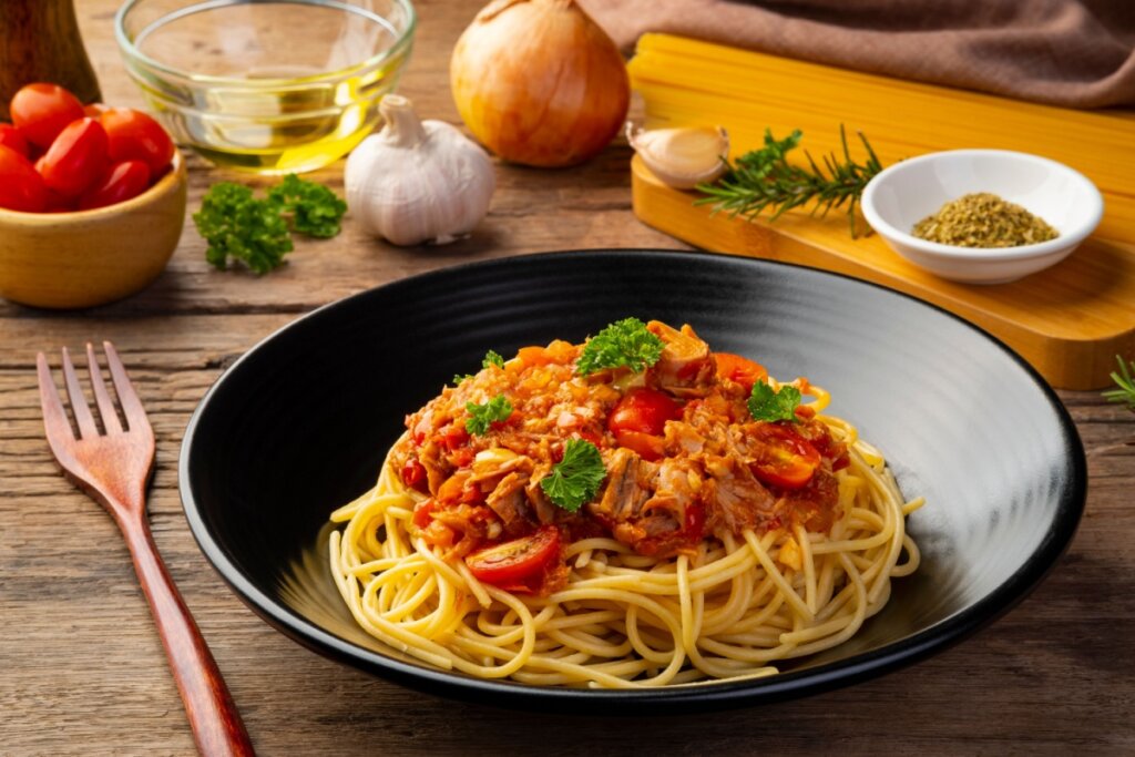 Espaguete com molho de atum servido em prato fundo preto em cima de mesa de madeira
