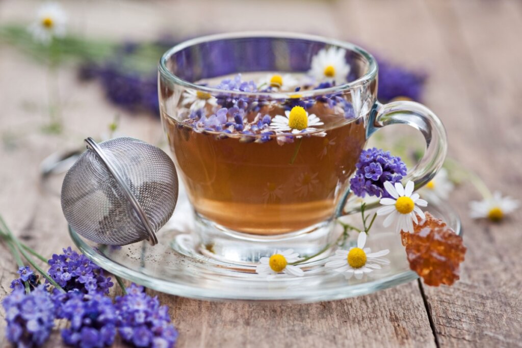 xícara de vidro com chá com folhas de camomila e lavanda. ao lado da xícara, mais folhas de camomila e lavanda