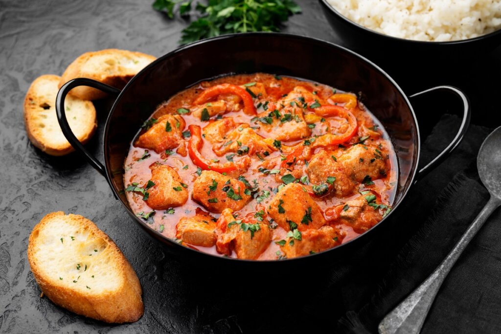 Moqueca de peixe com leite de coco em panela de ferro em cima de mesa preta com torradas ao redor