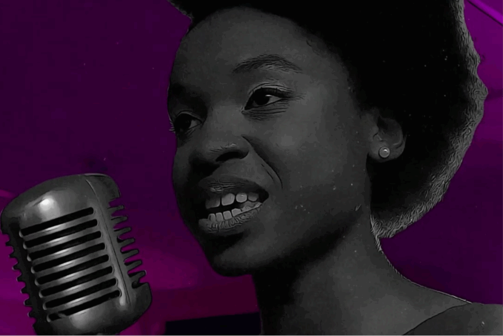 Jovem mulher negra sorrindo enquanto canta ao lado de um microfone, em imagem preto e branco sobre fundo roxo