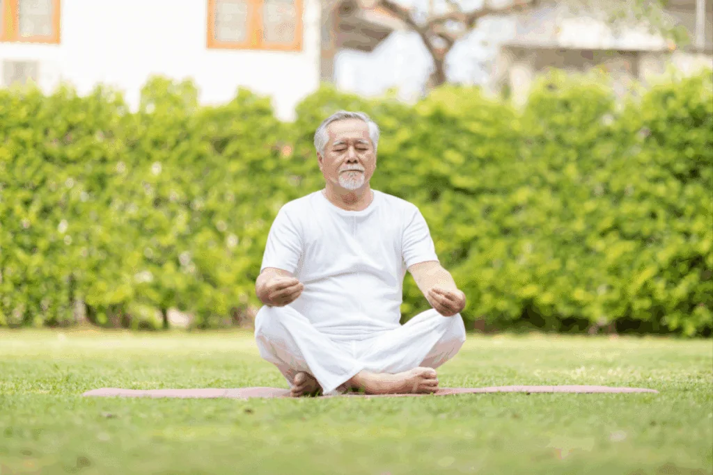 Homem de meia-idade, usando camisa e calça branca, meditando em um jardim