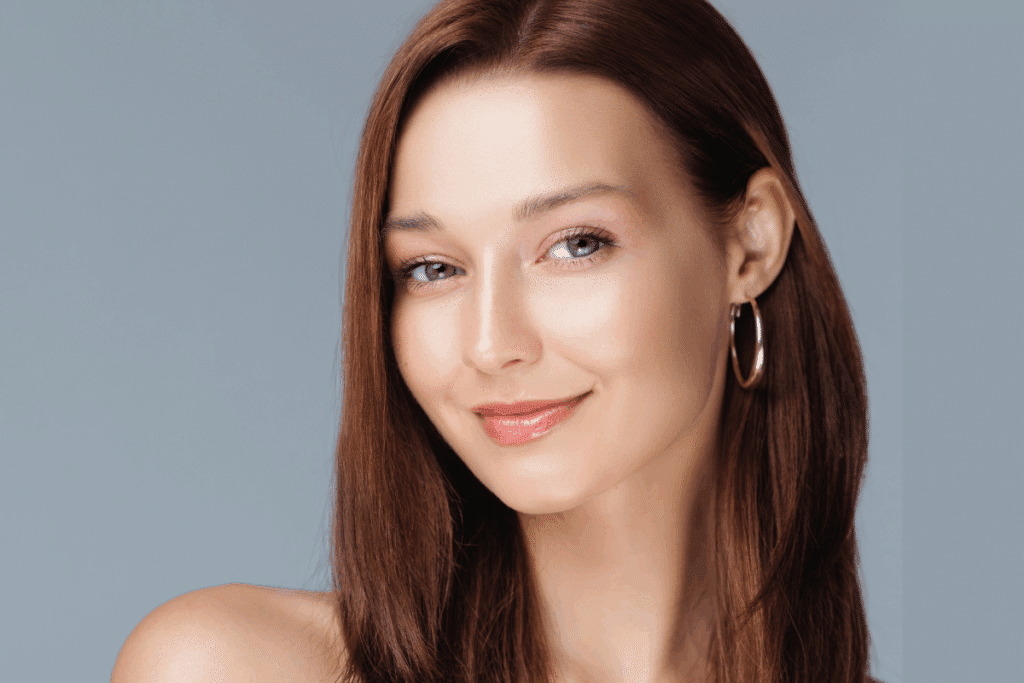 Mulher de pele clara com cabelo liso na cor castanho-avermelhado (Burnt Copper), maquiagem suave e brincos de argola.