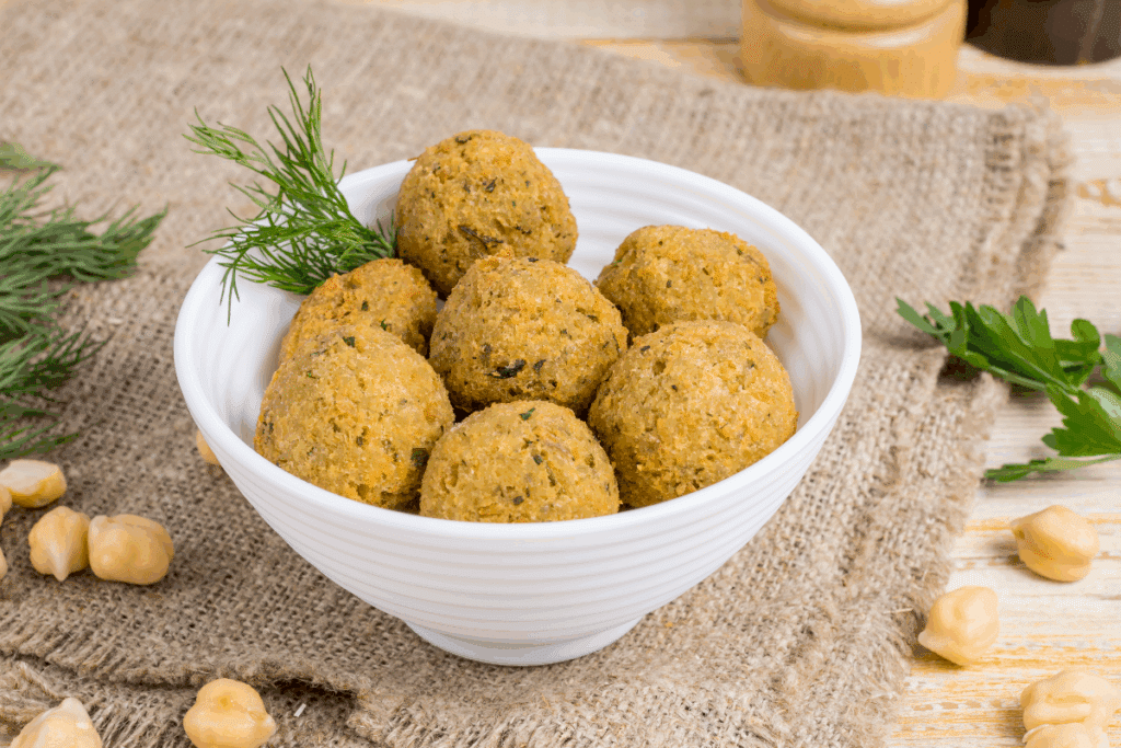 Bolinho de grão-de-bico servido em tigela branca em cima de mesa de madeira com grão-de-bico ao redor