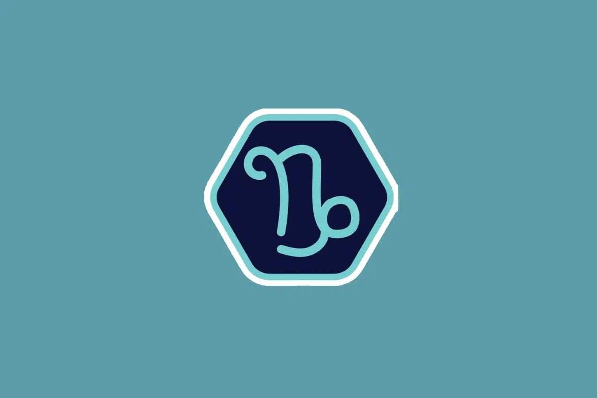 Ilustração minimalista do símbolo do signo de capricórnio em tom azul-claro, centralizada dentro de um hexágono azul-escuro com borda branca e azul. O fundo da imagem é em um tom sólido de azul-turquesa
