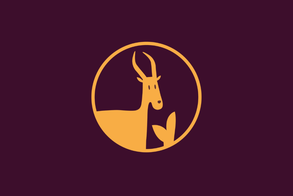 Ícone ilustrado em tom amarelo sobre fundo roxo escuro, dentro de uma moldura circular, representando o signo de Capricórnio através do busto de uma cabra com cornos pontiagudos e uma cauda ao lado