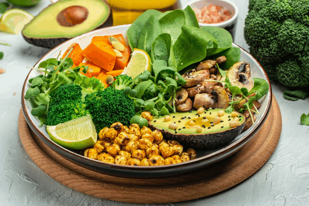 Prato fundo com salada de abacate, cogumelos refogados, brócolis, espinafre, abóbora assada, grão-de-bico tostado, microverdes e gomos de limão sobre tábua de madeira